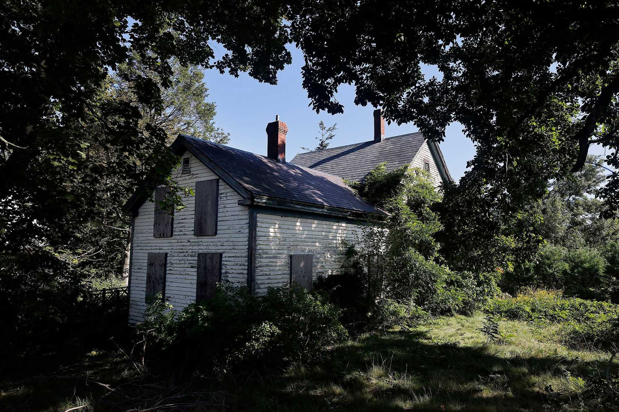 Milton, MA.  09/14/23 -   One of the boarded-up buildings of Milton’s poor farm decays beneath a tangle of nature.  Governor William Stoughton (1631–1701) bequeathed Milton 40 acres of land intended for the poor.  It hasn’t worked out that way.  Much of the land was sold to a developer, and now multimillion dollar homes sit on the land.  Only a small portion remains.  The roots of the region’s housing issues lie in zoning laws that were passed, in some cases, before WWII.  Milton’s zoning requires single-family homes with few exceptions, making it a pleasant suburb, but exacerbating a housing shortage as well as traffic congestion.  (Lane Turner/Globe Staff) Reporter: (Patty Wen)  Topic: (xxhousingcrisis)