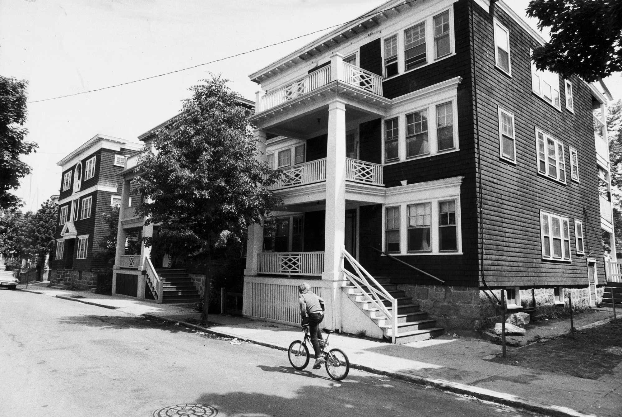 A boy on Melbourne Street in Dorchester in 1982 biked in front of triple-deckers, a type of housing banned in the early 20th century in many towns around Boston, including Milton.