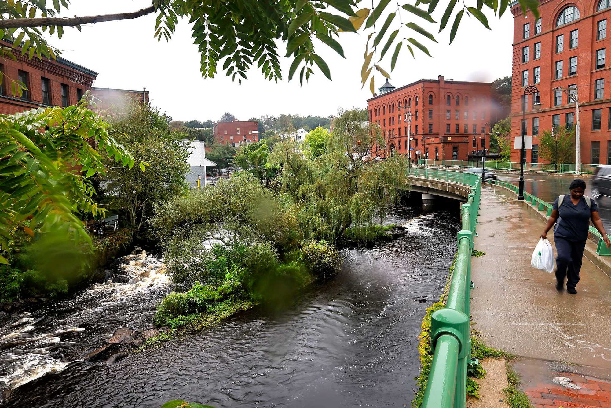 Milton, MA.  09/13/23 -  a pedestrian crosses the Adams Street Bridge over the Neponset River into Dorchester Lower Mills, a picturesque exit from a town facing a housing crisis.  The roots of the region’s housing issues lie in zoning laws that were passed, in some cases, before WWII.  Milton’s zoning requires single-family homes with few exceptions, making it a pleasant suburb, but exacerbating a housing shortage as well as traffic congestion.  (Lane Turner/Globe Staff) Reporter: (Patty Wen)  Topic: (xxhousingcrisis)