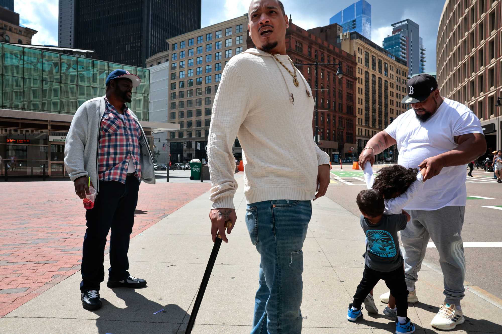 Milton DoSouto (center) took in the scene while his brother, Mike Fernandes, entertained children, at City Hall Plaza in May 2024. Family and friends had gathered at Suffolk County Superior Court to attend a hearing for Odair Fernandes.  
