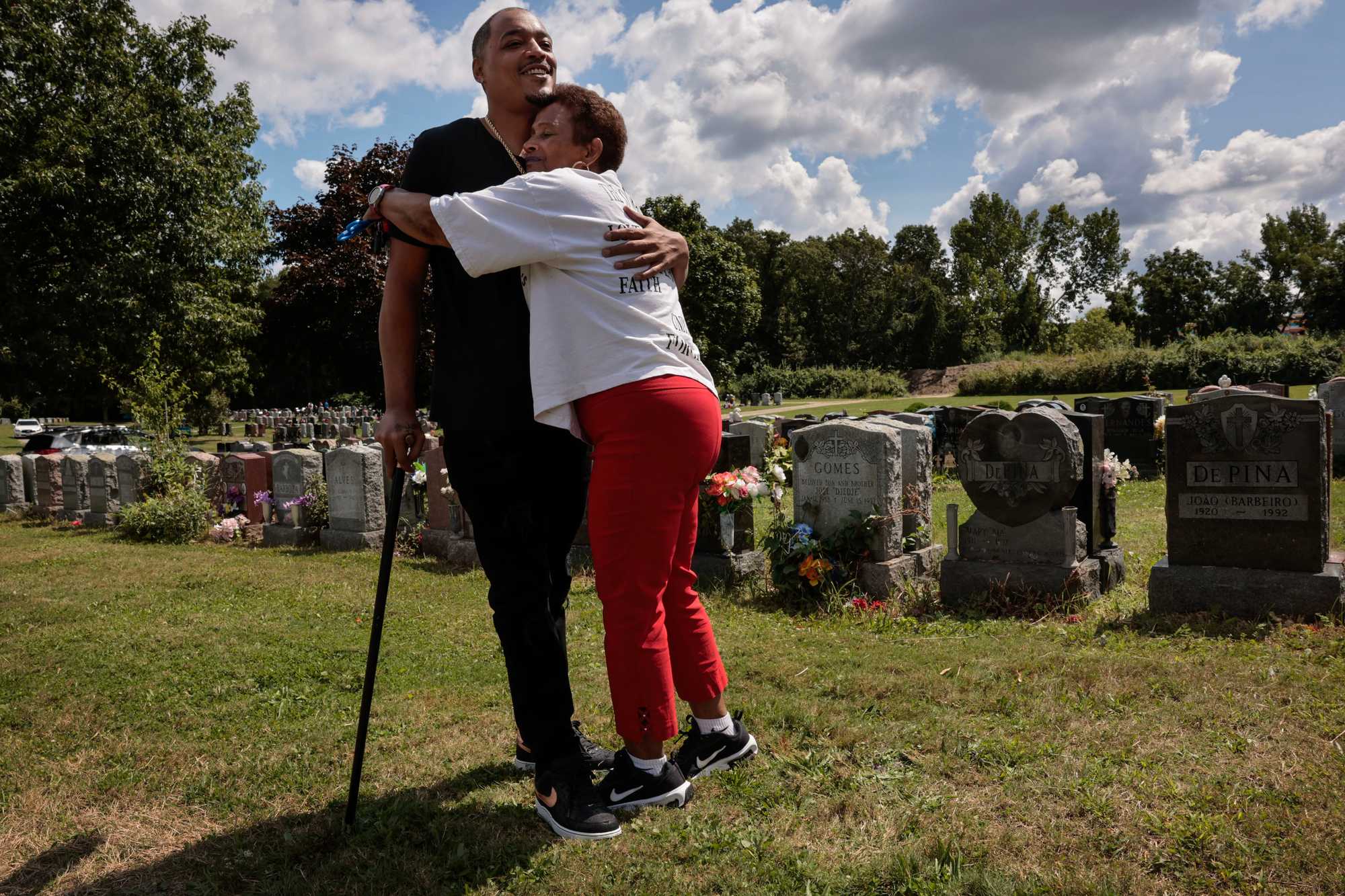 Isaura Mendes greeted Milton DoSouto near the graves of her sons Bobby and Matthew, who were killed amid gang warfare in Dorchester. The 74-year-old Mendes has become a peace advocate for her community alongside DoSouto, who has two brothers — Luis and Alex — buried at the New Calvary Cemetery in Mattapan, both killed by gunfire. (Craig F. Walker/Globe staff)