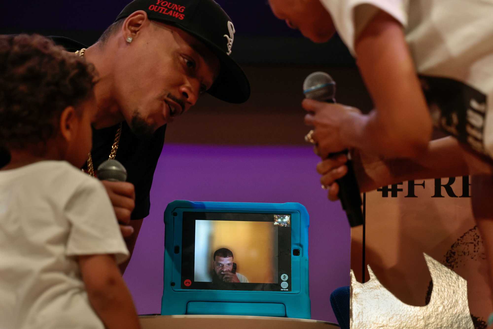 Odair Fernandes spoke over a video feed during the "Tudo Djunto: All Together We Can End the Violence" community forum at the Boston Public Library while Milton DoSouto, his son Alex, and Fernandes's wife, Deanna, gathered around.