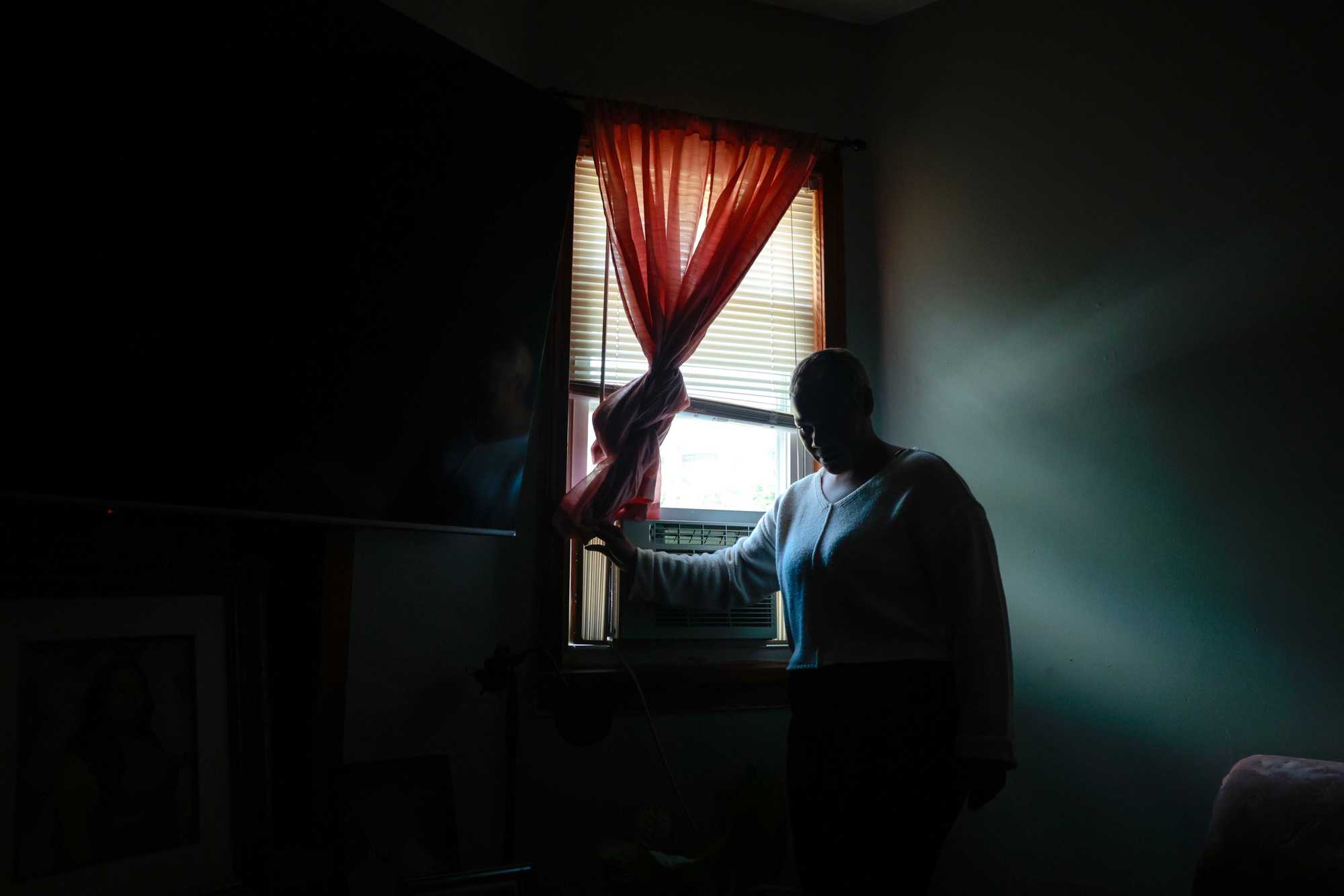 Christina DoSouto stood in her family's living room in their home on Hamilton Street in June. Her mother, Luisa, used to look out the window at the spot where her son Luis was fatally shot. (Craig F. Walker/Globe staff) 