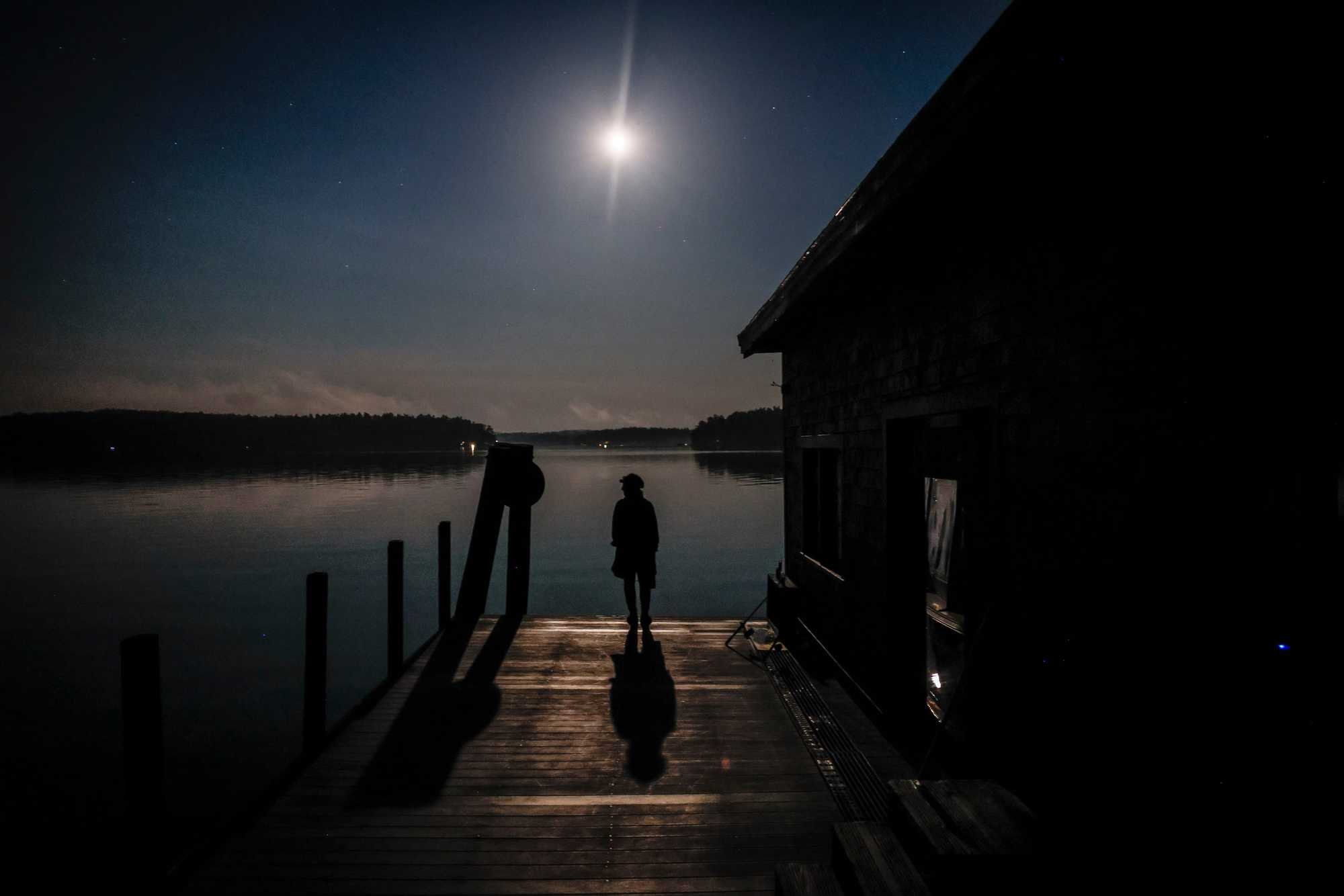 A camper stands on the dock under a full moon at Miles of Music Island Camp on Lake Winnipesaukee.