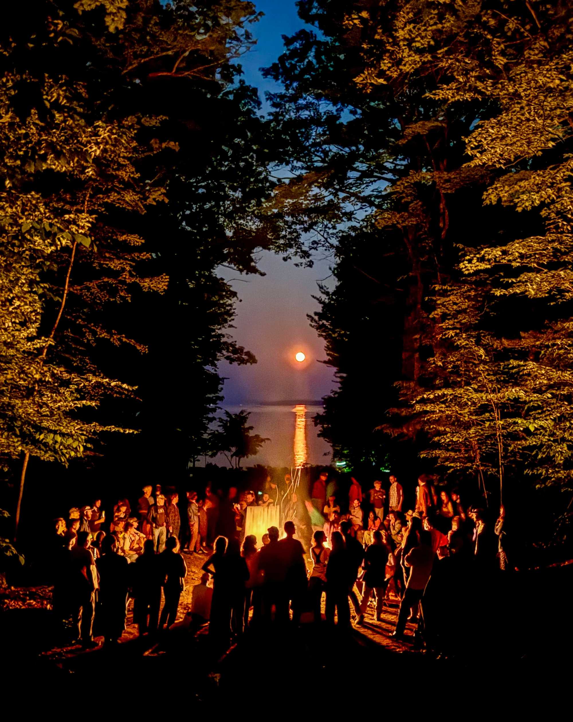 Campers gather around a bonfire under a strawberry moon.