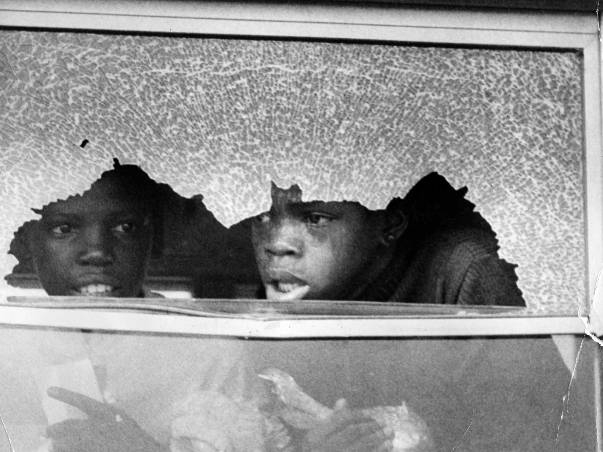Two young Boston students look out a broken window on their bus in September 1974.