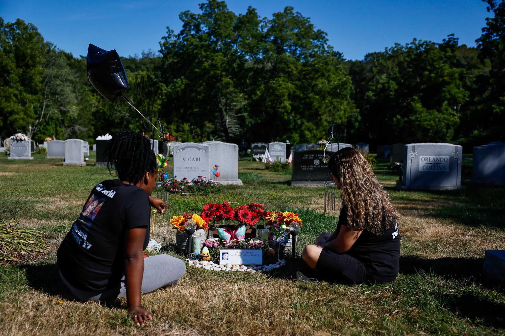 Tyla Ordonez (left) and Skye Foote sat at the grave site of their friend G Araujo in Gloucester. Araujo died in 2018 after running away from a group home. (Erin Clark/Globe staff)