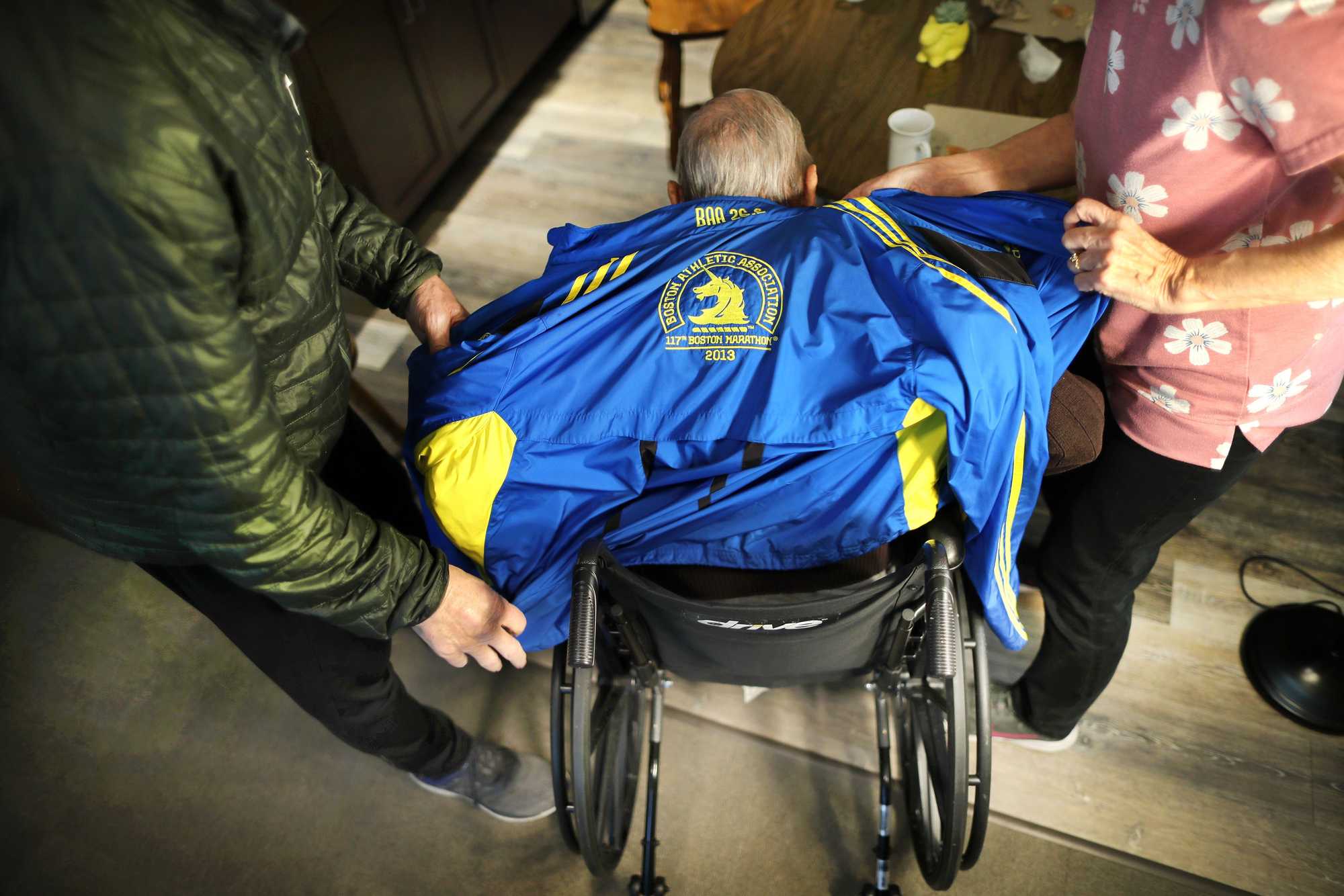 Boston Marathon veteran Bill Iffrig got help with his jacket from his son Mark and daughter Susan at Fieldstone Memory Care as they prepared to go outside. He has worn it all the time for the last 10 years.