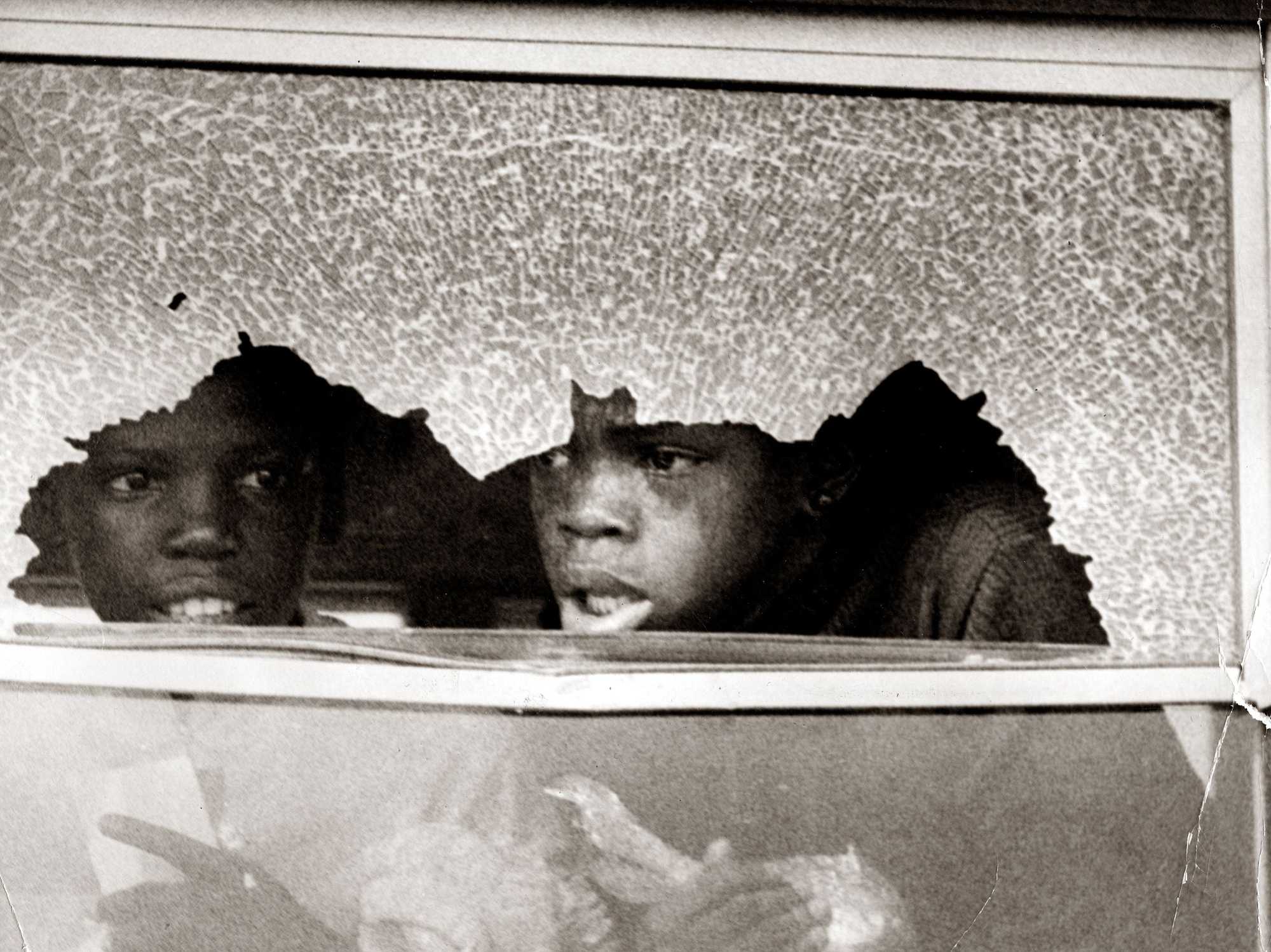 Two Boston students looked out of a broken school bus window on Sept. 12, 1974. (Boston Globe Archive)