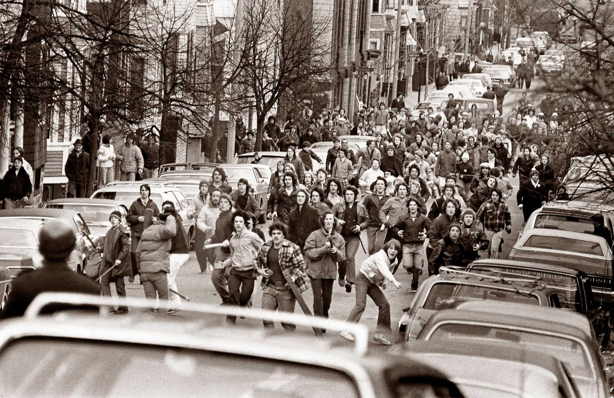 A crowd of antibusing demonstrators stormed up East Sixth Street in South Boston, armed with rocks and clubs on Feb. 15, 1976. A demonstration erupted into two hours of bitter street fighting between protestors and police, who used tear gas to disperse the crowd. (Ulrike Welsch/Globe Staff) 