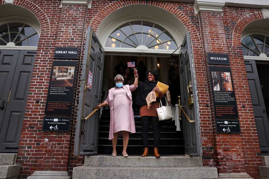 (For Brian Macquarrie story on  Peter Faneuil) Boston,MA - 2/16/2023: Sedelia Jean-Michel, 78, left, of Stoughton, raises an American flag with her daughter, Regine Francois following a Naturalization Ceremony in the Great Hall of Faneuil Hall in Boston, MA on February 16, 2023. Sedelia came to the states from Haiti twenty years ago.  (Craig F. Walker/Globe Staff) Peter Faneuil