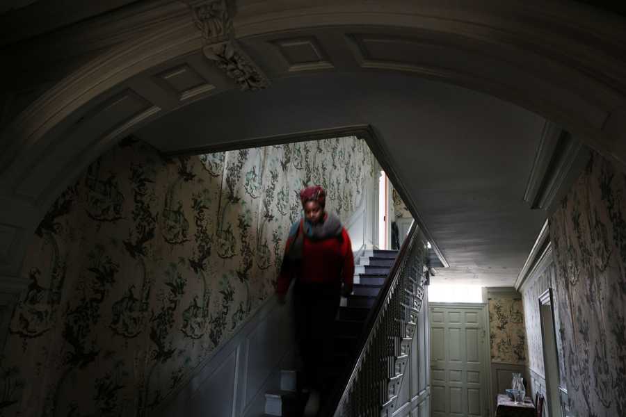 Medford, MA - 2/21/2023: Executive Director Kyera Singleton descends the staircase in the Big House while touring the Royall House and Slave Quarters in Medford, MA on February 21, 2023.(Craig F. Walker/Globe Staff) enslaved person Marble Chamber - kitchen chamber room - winter kitchen - dining room - parlor - 5 people slept in kitchen -  Isaac Royall Jr. (Sr.)