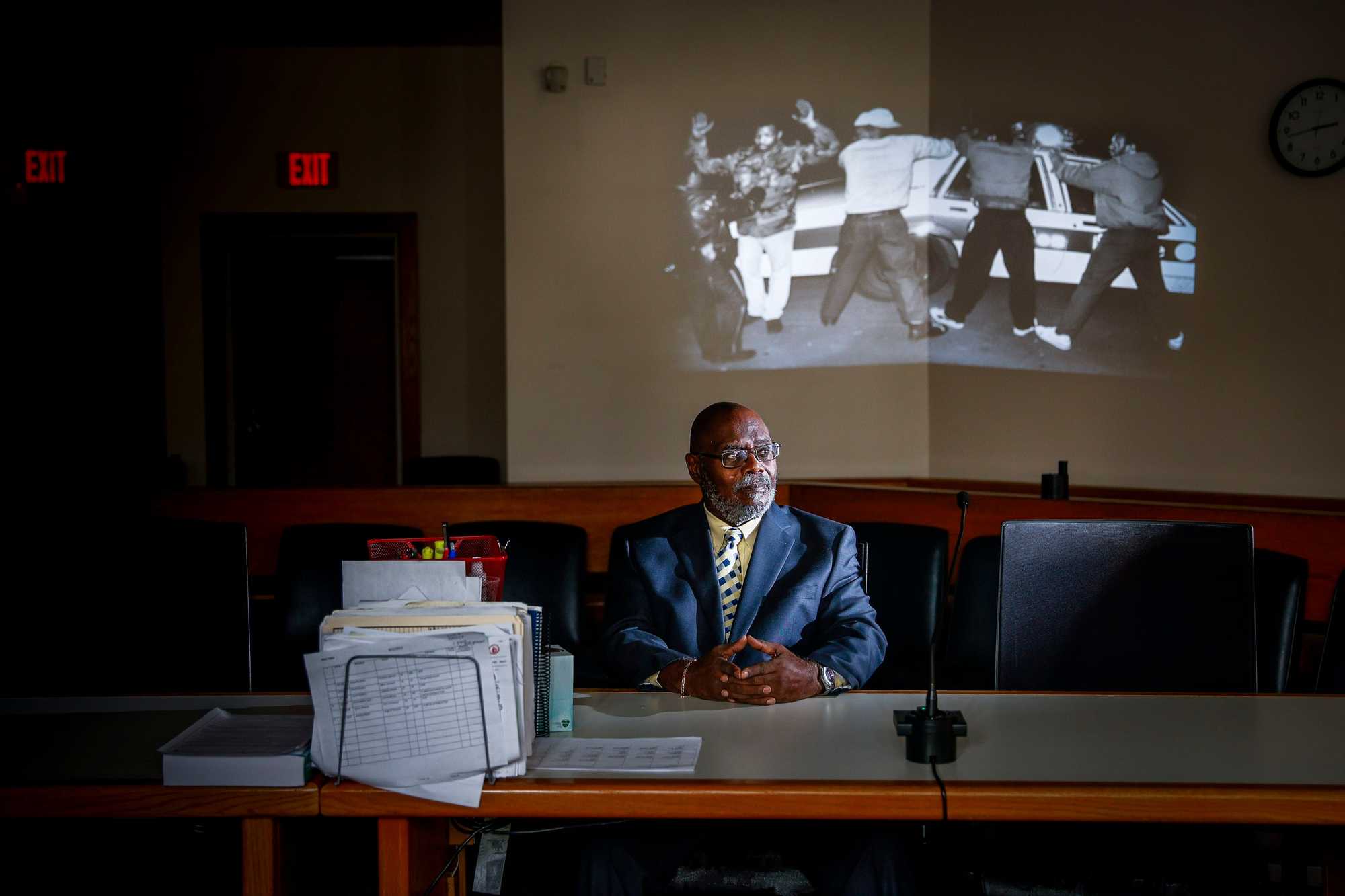 Retired judge Leslie Harris, sitting in front of a projected March 1989 photo of Boston police officers searching a group of men in the Roxbury neighborhood. Harris, a former public defender at the Roxbury Municipal Court, regularly represented young men of color from Mission Hill and was a lawyer for Alan Swanson, the first suspect wrongly linked to the Stuart shooting.