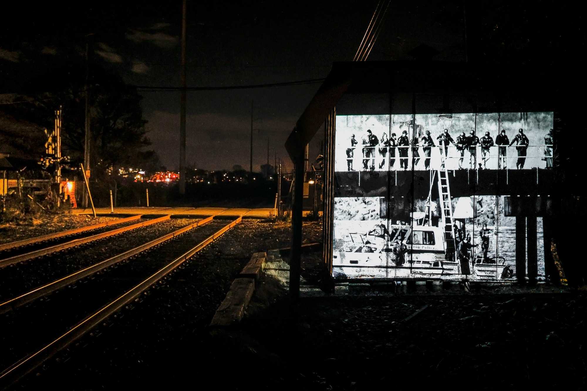 A photo from 1990 of the search for the murder weapon at the Pines River in Revere is projected near the train tracks leading to Dizzy Bridge.
