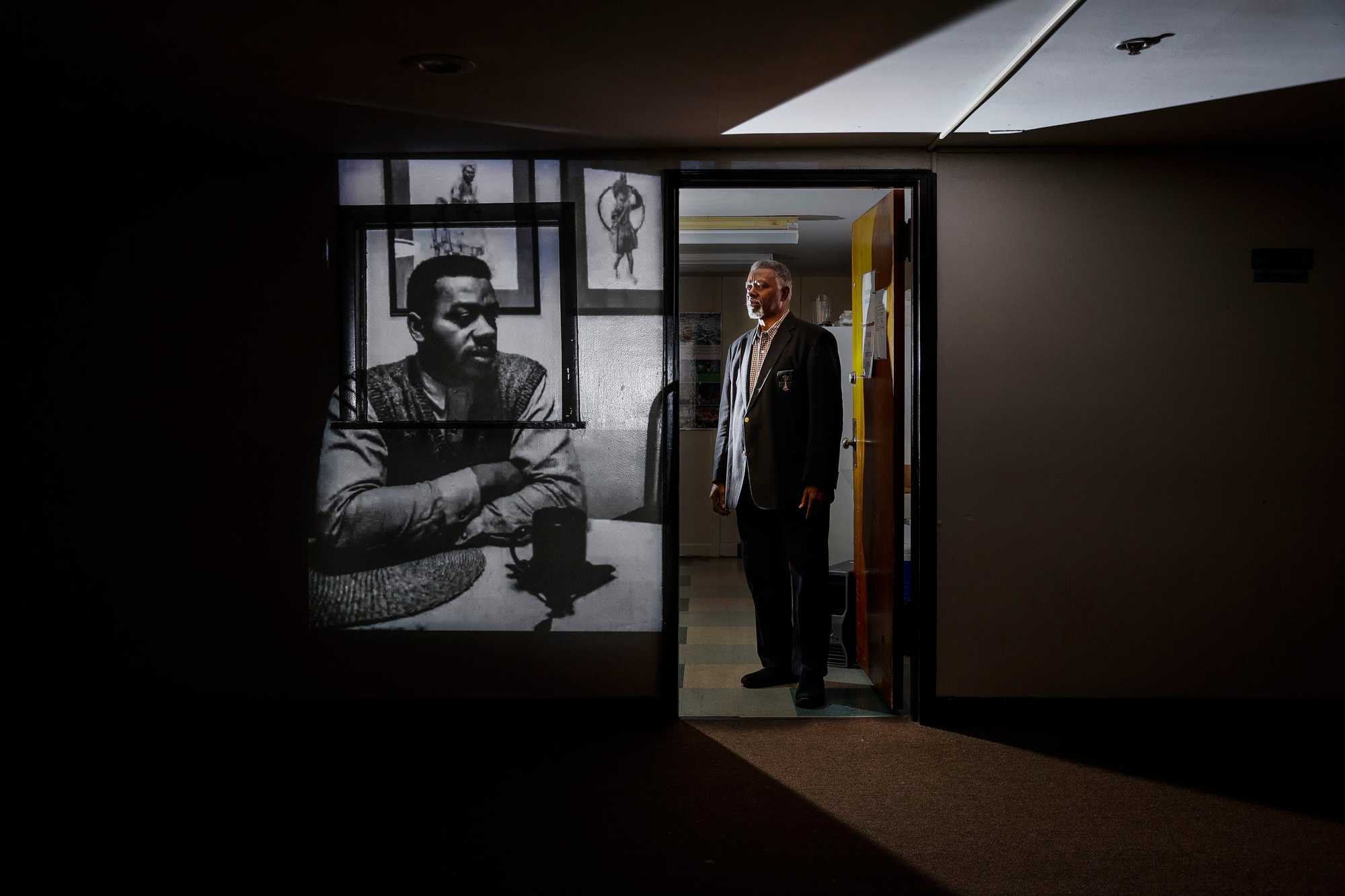  Louis Elisa, former president of the Boston chapter of the NAACP, standing at Prince Hall Grand Lodge near a projection of a photo himself speaking about the Stuart murder in 1990. Louis had been at a dinner of Free Masons when the shooting happened, and he headed straight to the Roxbury district police station after hearing the details. When he arrived, he saw officers already assembling with riot shields. 

