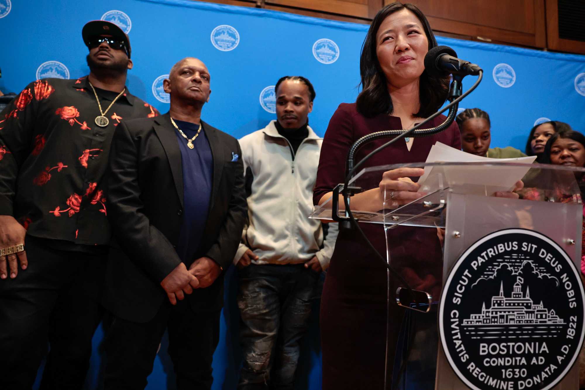 Boston, MA - 12/20/2023: Mayor Michelle Wu, right, addresses the crowd including Alan Swanson, second from left, and members of the Bennett family during a press conference and public apology to Swanson and Willie Bennett at City Hall in Boston, MA  on December 20, 2023. More than 34 years after Charles Stuart shot his pregnant wife and blamed a Black man for the crime, Mayor Michelle Wu issued a formal apology from the city to two men who were wrongly linked to the shooting, Alan Swanson and Willie Bennett.  (Craig F. Walker/Globe Staff)