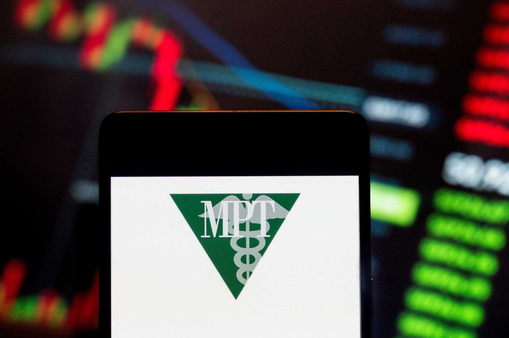 In this photo illustration, the logo of Medical Properties Trust, a real estate investment trust that invests in health care facilities, was displayed on a smartphone with an economic stock exchange index graph in the background. 