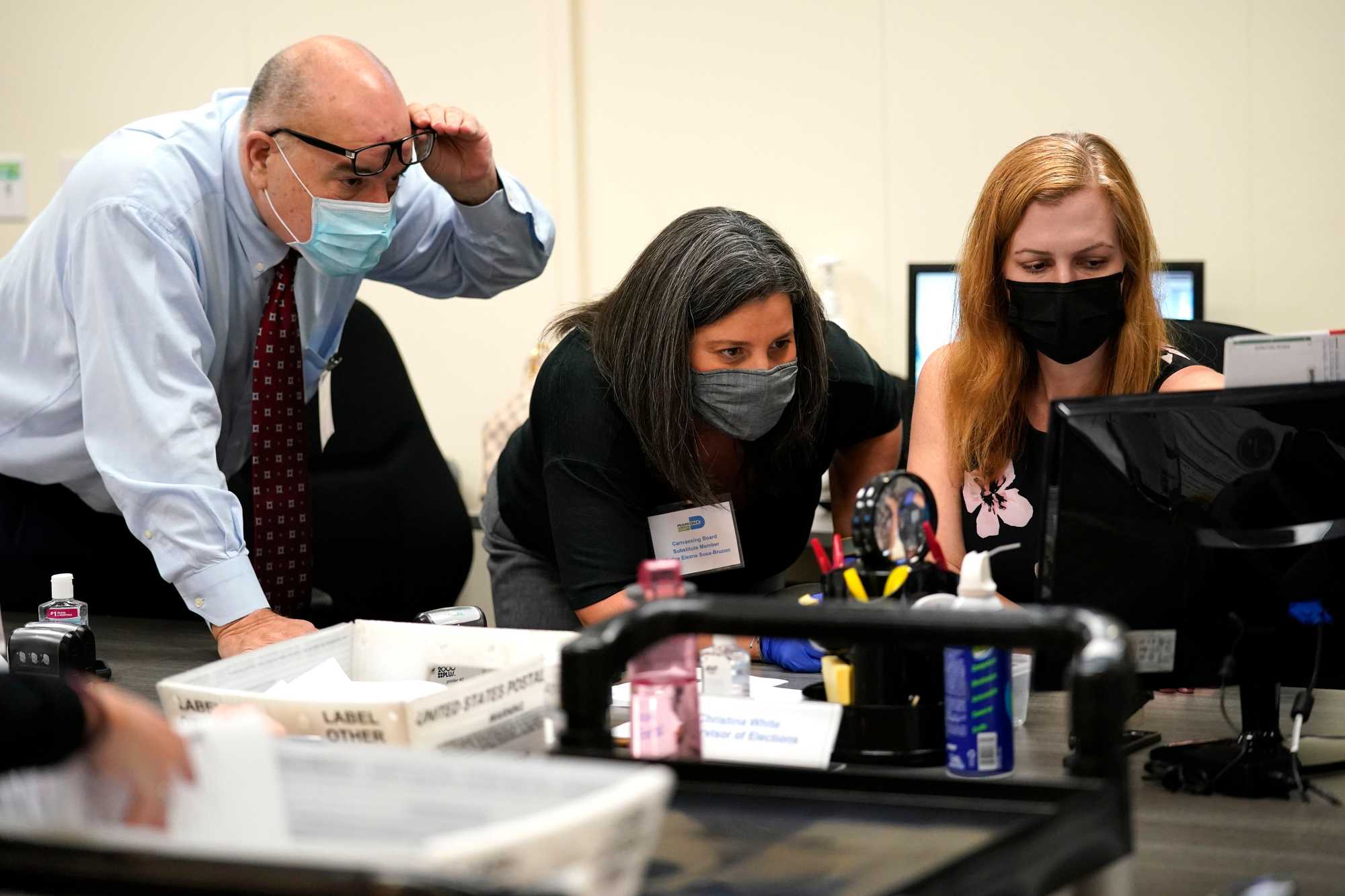 Miami-Dade County Supervisor of Elections Christina White (right) examined signatures on vote-by-mail ballots with members of the Canvassing Board Judge Raul Cuervo (left) and Judge Betsy Alvarez-Zane at that county's Board of Elections in Doral, Fla. on Oct. 26, 2020.