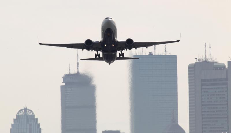 Front view of a plane taking off from Boston Logan airport with residential buildings in the background.
