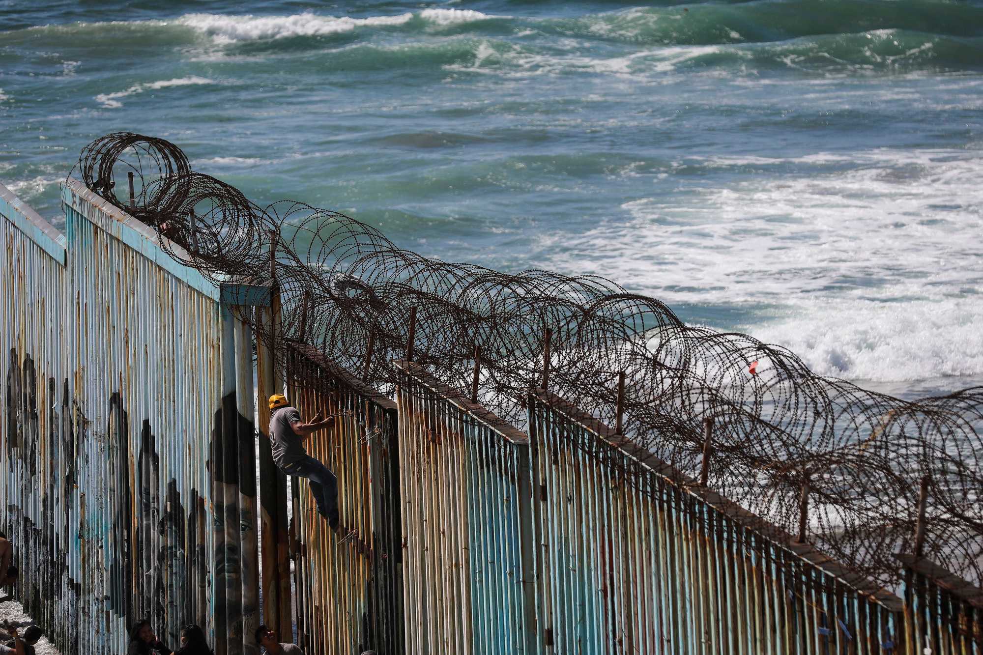 A man climbed partially up the Mexico side of the border wall for a photo opportunity in Tijuana. 