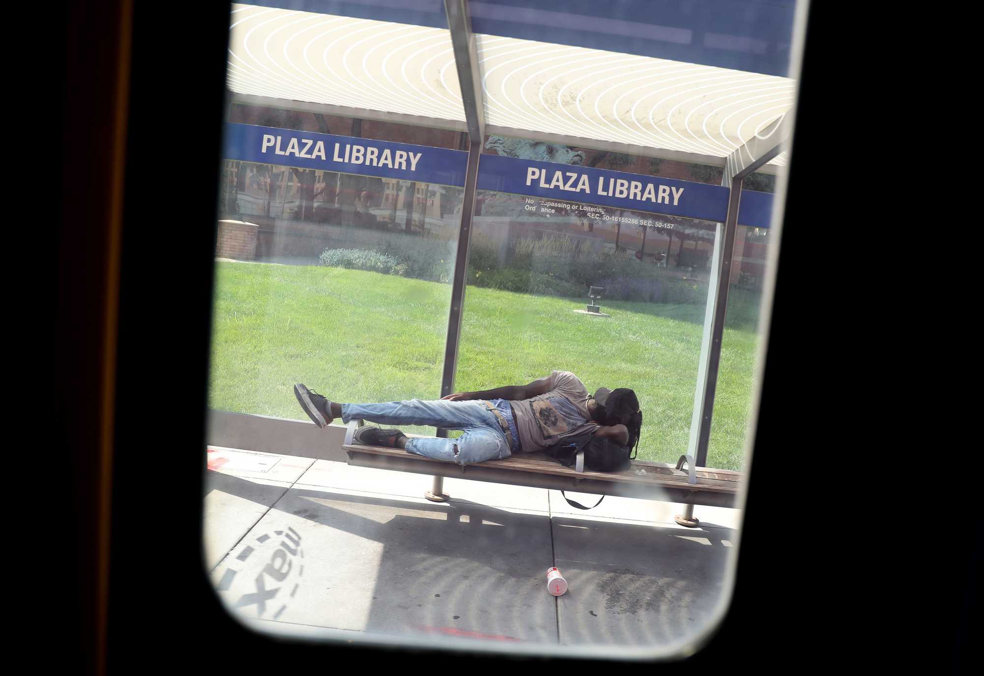 A bus window framed a person napping on a Plaza Library bench in Kansas City.  