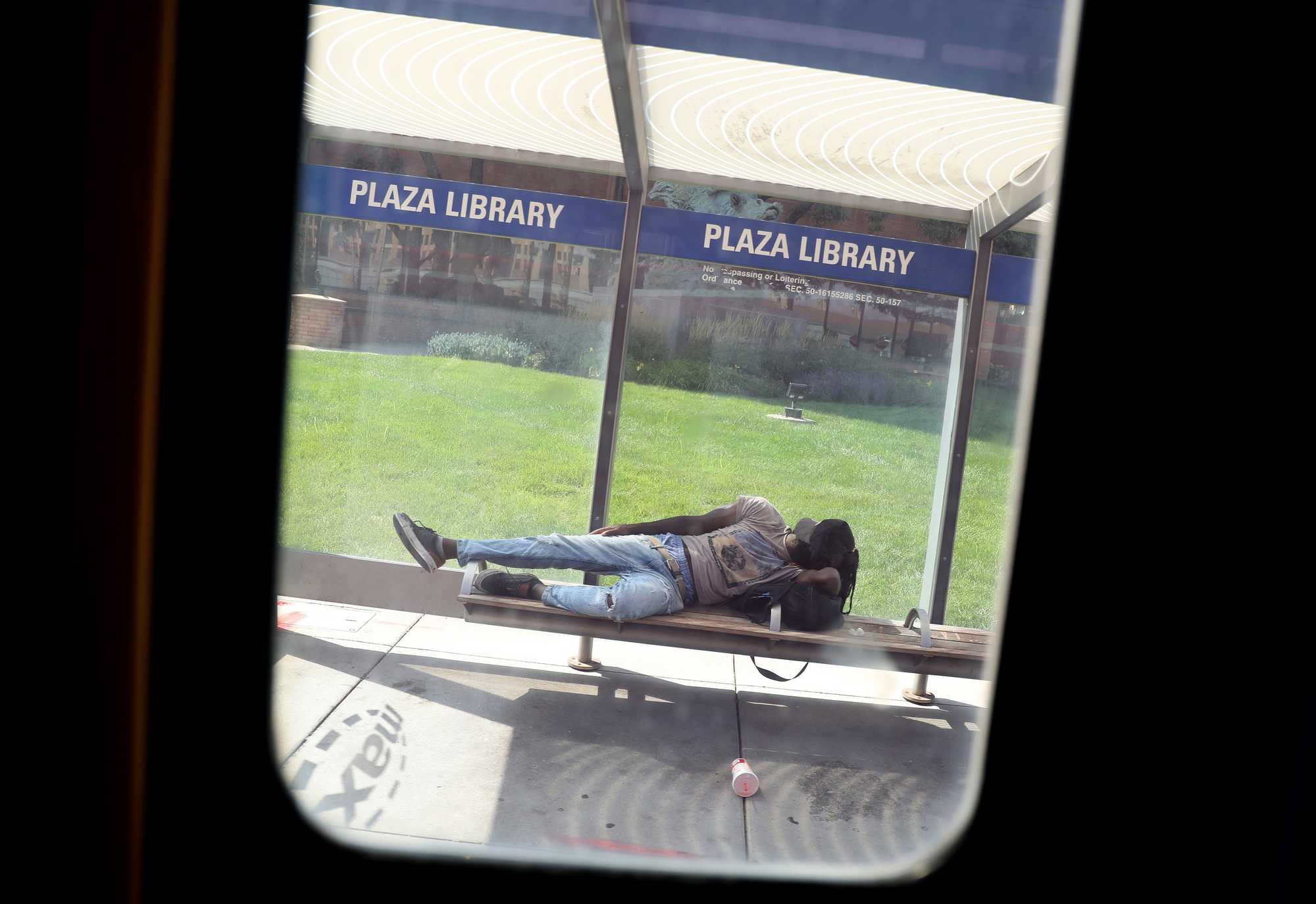 A bus window framed a person napping on a Plaza Library bench in Kansas City.