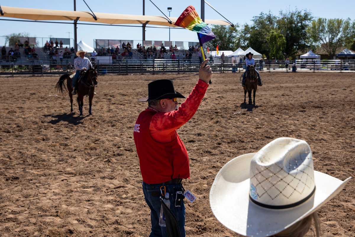 A rodeo judge held a rainbow flag during the Chute Dogging  competition.