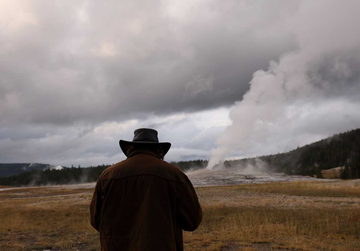 A man bent to take a video as steam rose from Old Faithful in Yellowstone National Park.