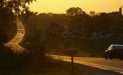 A climbing Iowa road and power lines are lit by the late sun.