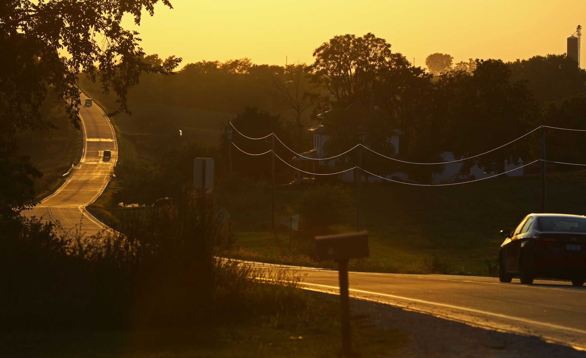 A climbing Iowa road and power lines were lit by the late sun. 